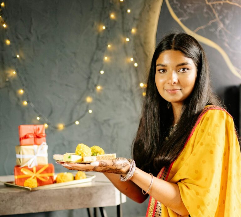 A young woman in traditional attire holding a tray of sweets during Diwali celebration indoors.